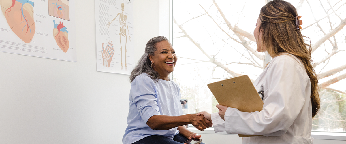 Woman shaking hands with a healthcare professional in a doctor's office.