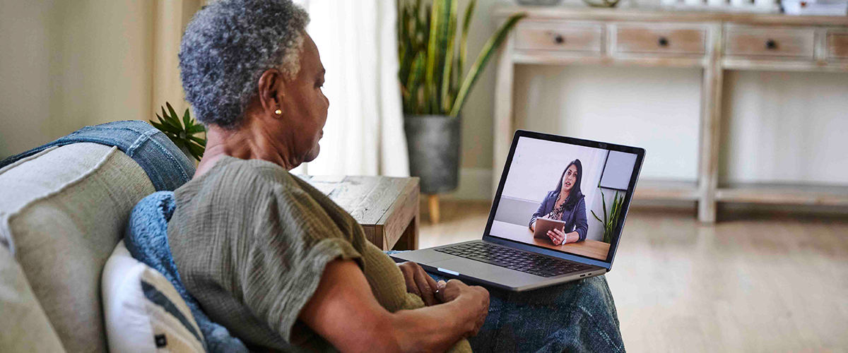 Woman sitting on the couch at home, attending a telehealth appointment on a laptop computer.